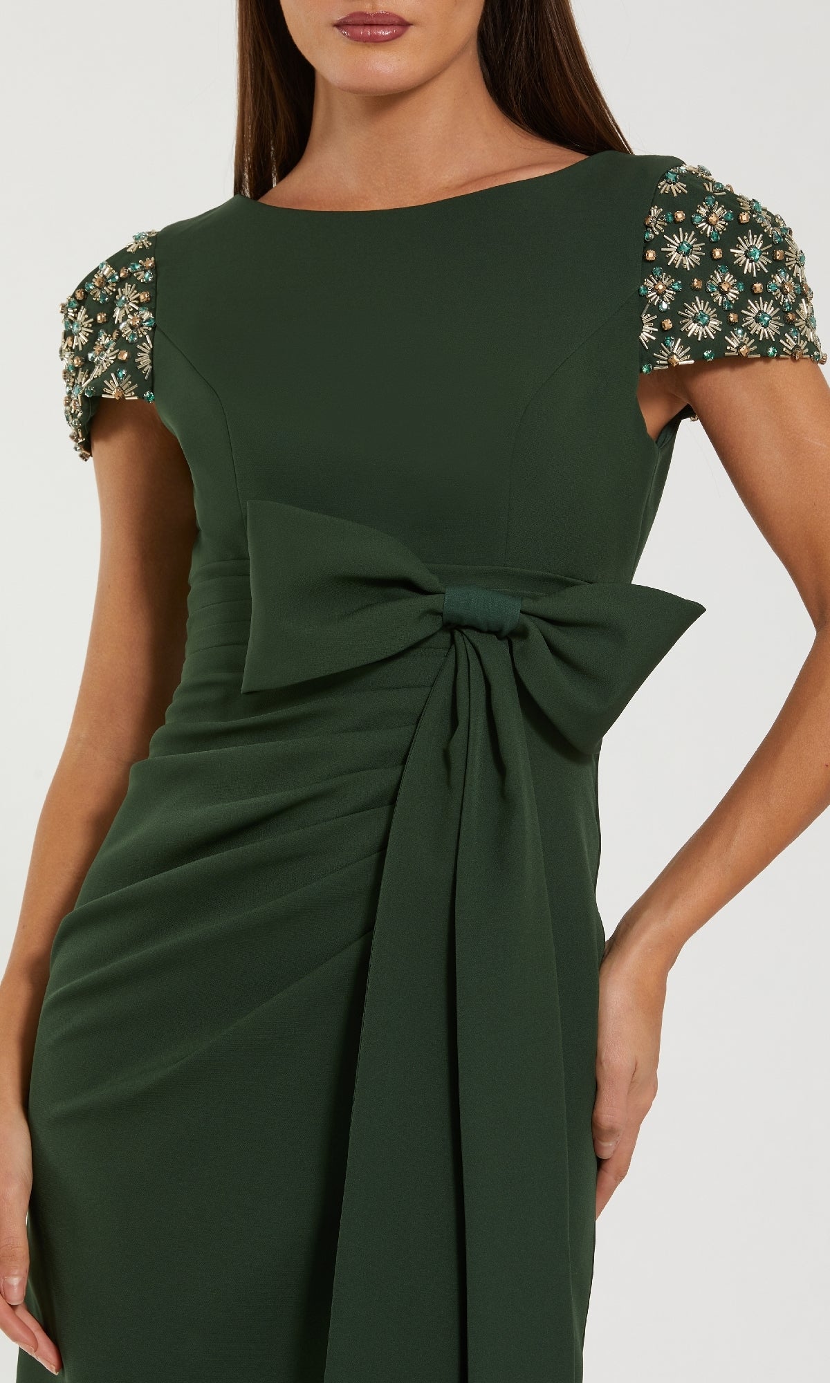 Woman in a Mac Duggal 50054 long formal dress in dark green, featuring beaded cap sleeves and a large bow accent at the waist.
